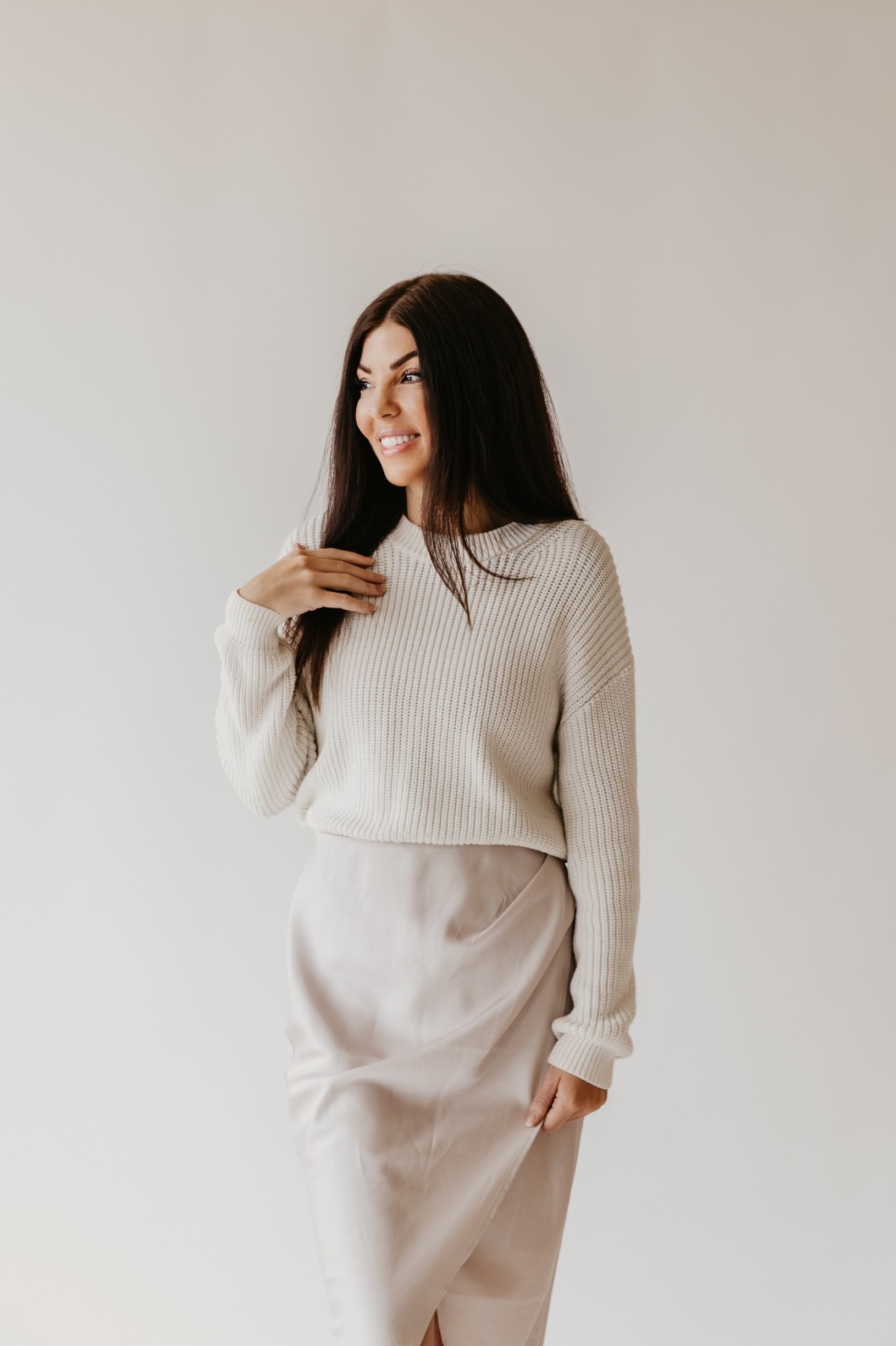Alyssa wearing a cream knit sweater and satin skirt